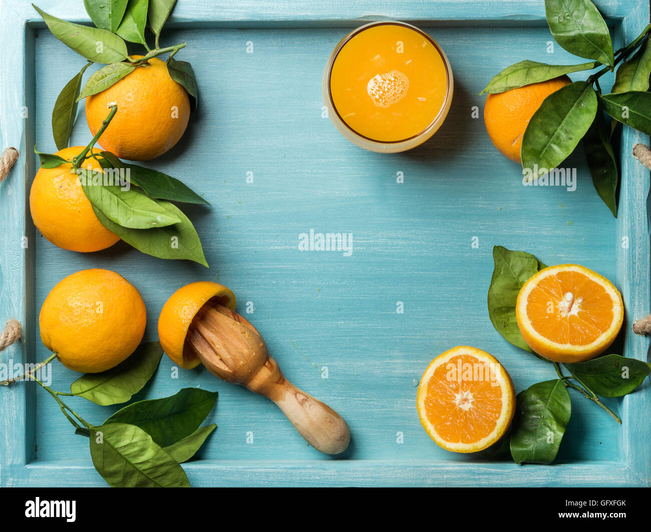 Frischer gepresster Orangensaft aus Glas und Orangen mit Blätter auf hölzernen Türkis Blau bemalten Hintergrund Stockfoto