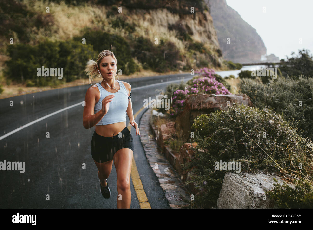 Fitness-Frau läuft auf Autobahn um die Berge. Sportlerin Training im Freien bei Regen. Stockfoto