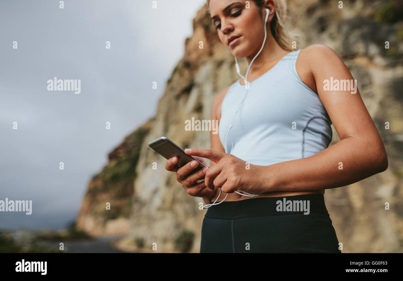 Junge weibliche Läufer eine Pause und Musikhören während des Laufs im Freien. Junge Frau mit Blick auf Mobile Kopfhörer Stockfoto