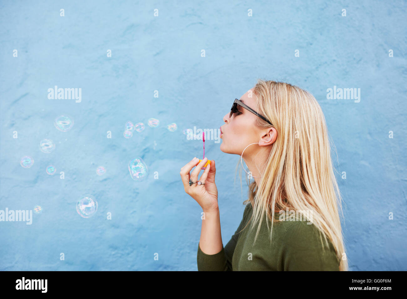 Richtungskontrolle Blick des jungen schönen Frau Seifenblasen vor blauem Hintergrund. Junge, blonde Frau Spaß zu haben. Stockfoto