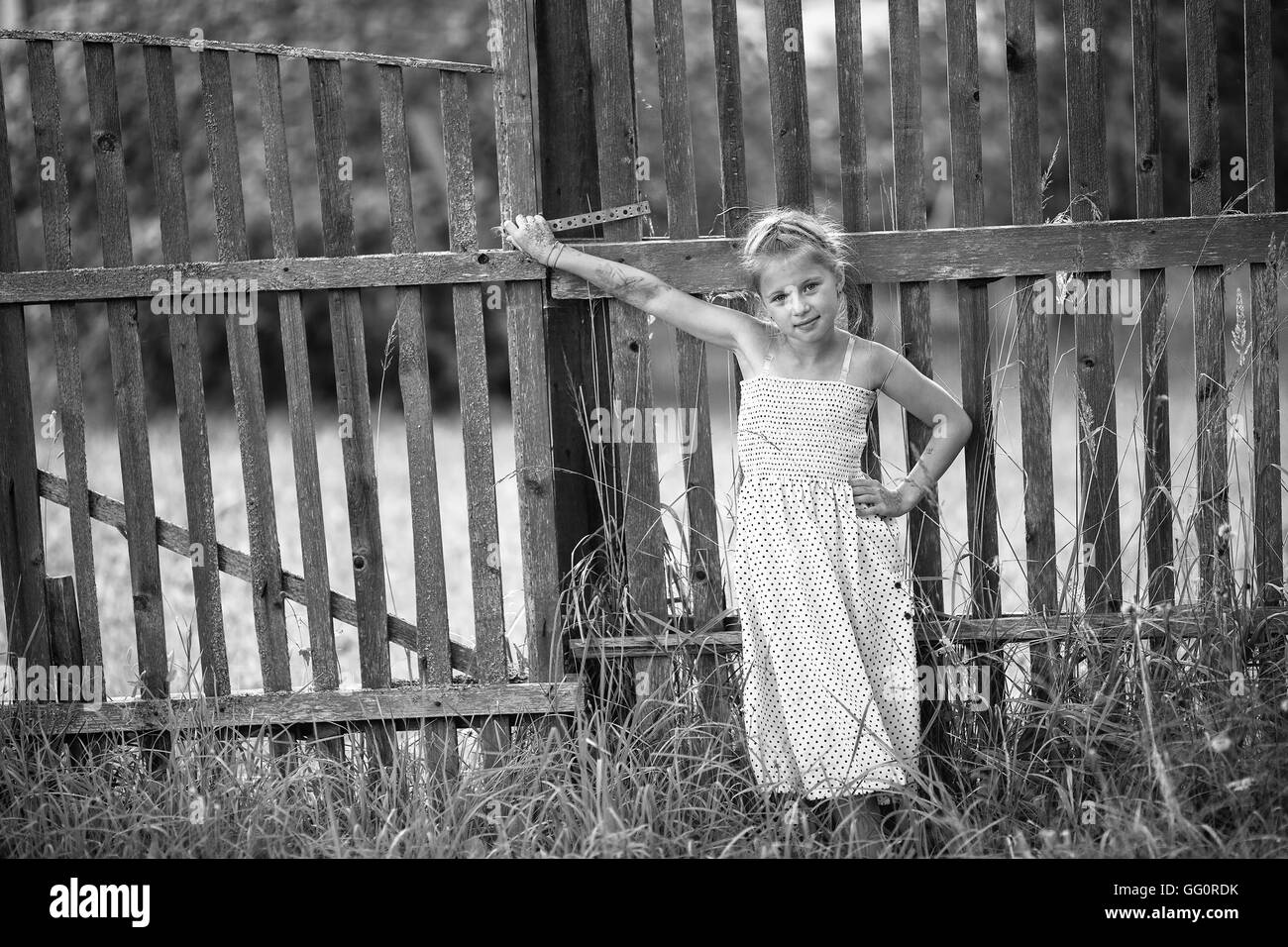 Niedliche kleine Mädchen steht in der Nähe einen Zaun im Dorf. Schwarz / weiß Foto. Stockfoto