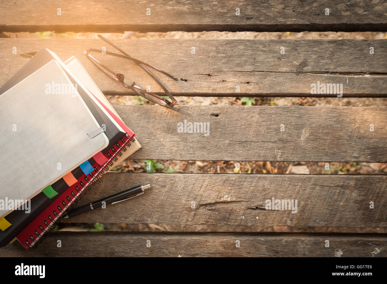 Stift, geöffneten Notizbuch, Gläser und Kaffeetasse auf Holz Gartentisch in Morgen am Wochenende. Freier Wirtschaftsjournalist arbeiten Leben Stockfoto