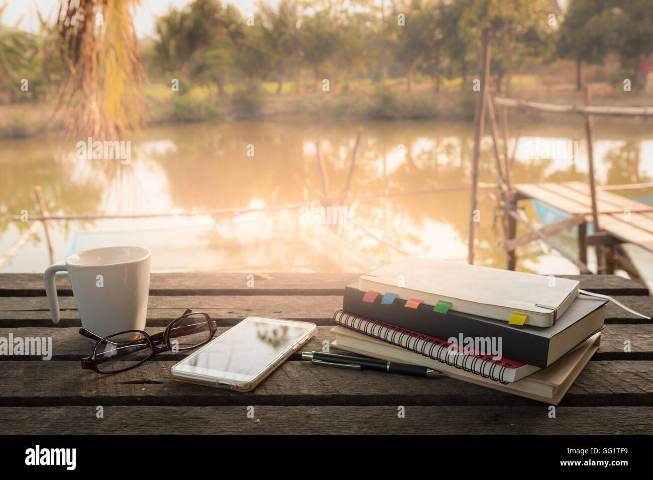 Smartphone, Notebooks, Kaffeetasse, Gläser und Stift legte auf Holz Gartentisch in Morgen am Wochenende. Freiberuflicher busines Stockfoto