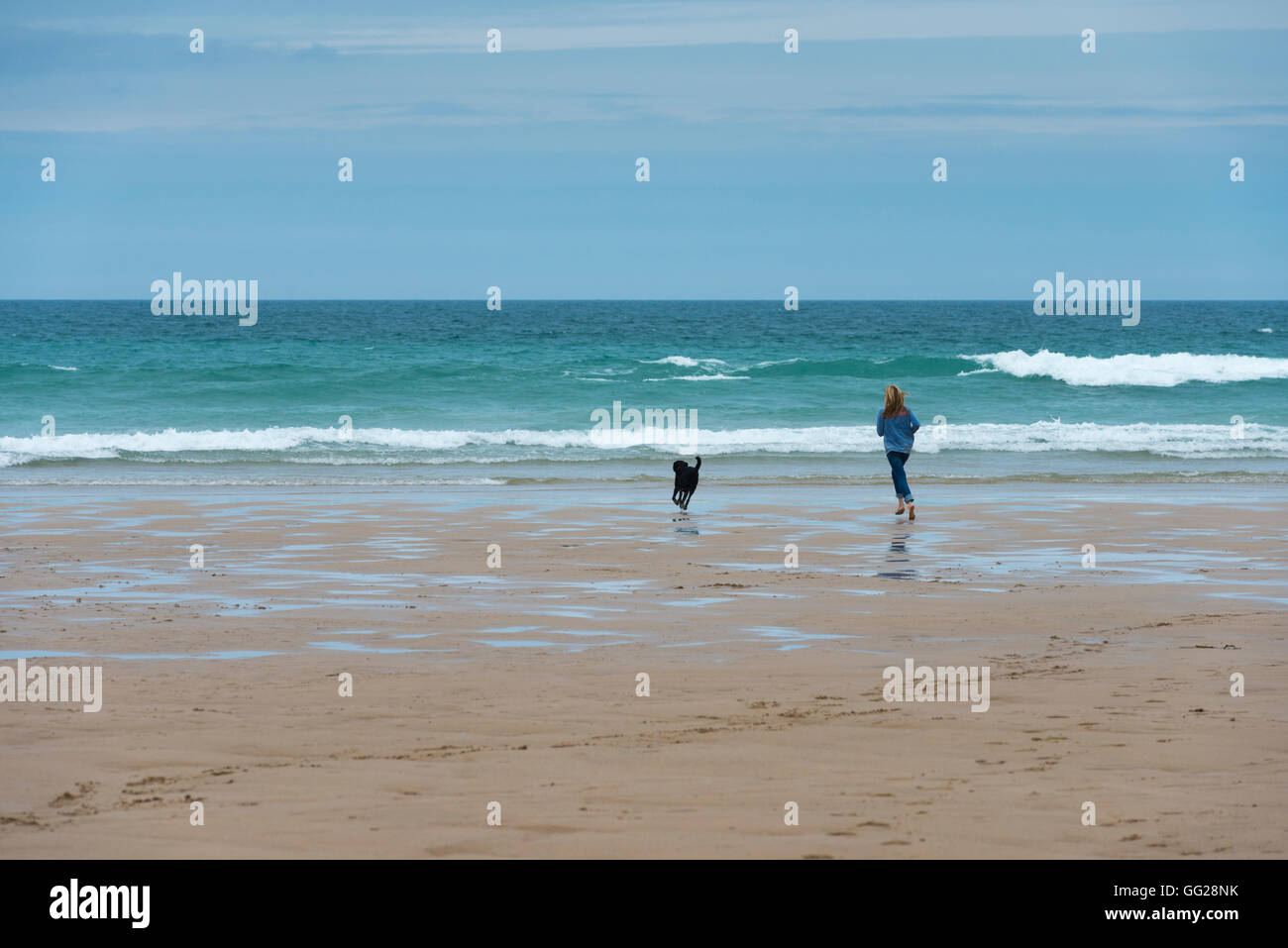 Eine Frau mit einem Labrador Hund läuft an einem Strand in Cornwall UK Stockfoto