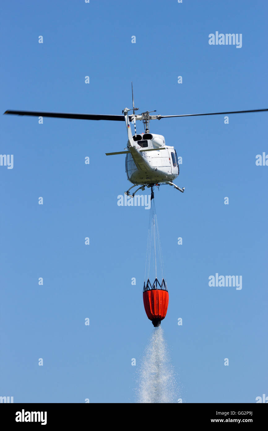 Hubschrauber mit einem Bambi-Eimer mit Wasser gefüllt um einen Waldbrand zu bekämpfen Stockfoto