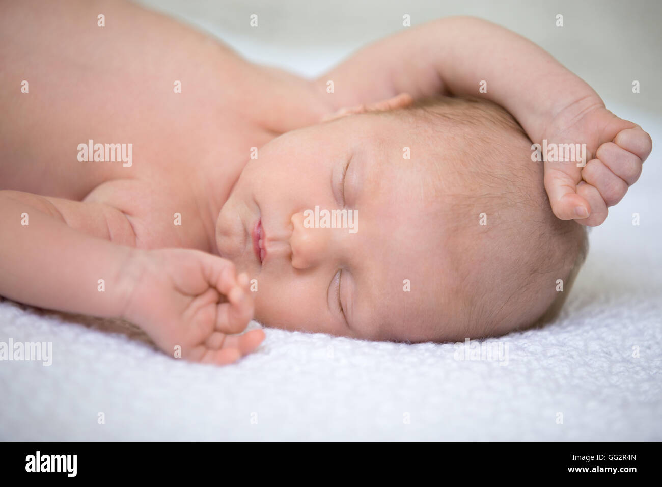 Portrait von junge lustige Neugeborene Babe Nickerchen auf weichen weißen gestrickte Decke mit seinen Armen auf. Süße kaukasische neugeborenes Kind schlafen Stockfoto
