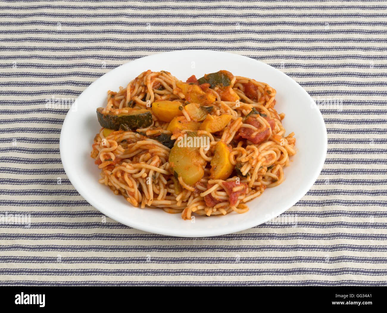 Angel Hair Pasta mit Zucchini und Spinat auf einem weißen Teller oben auf eine gestreifte Tischdecke. Stockfoto