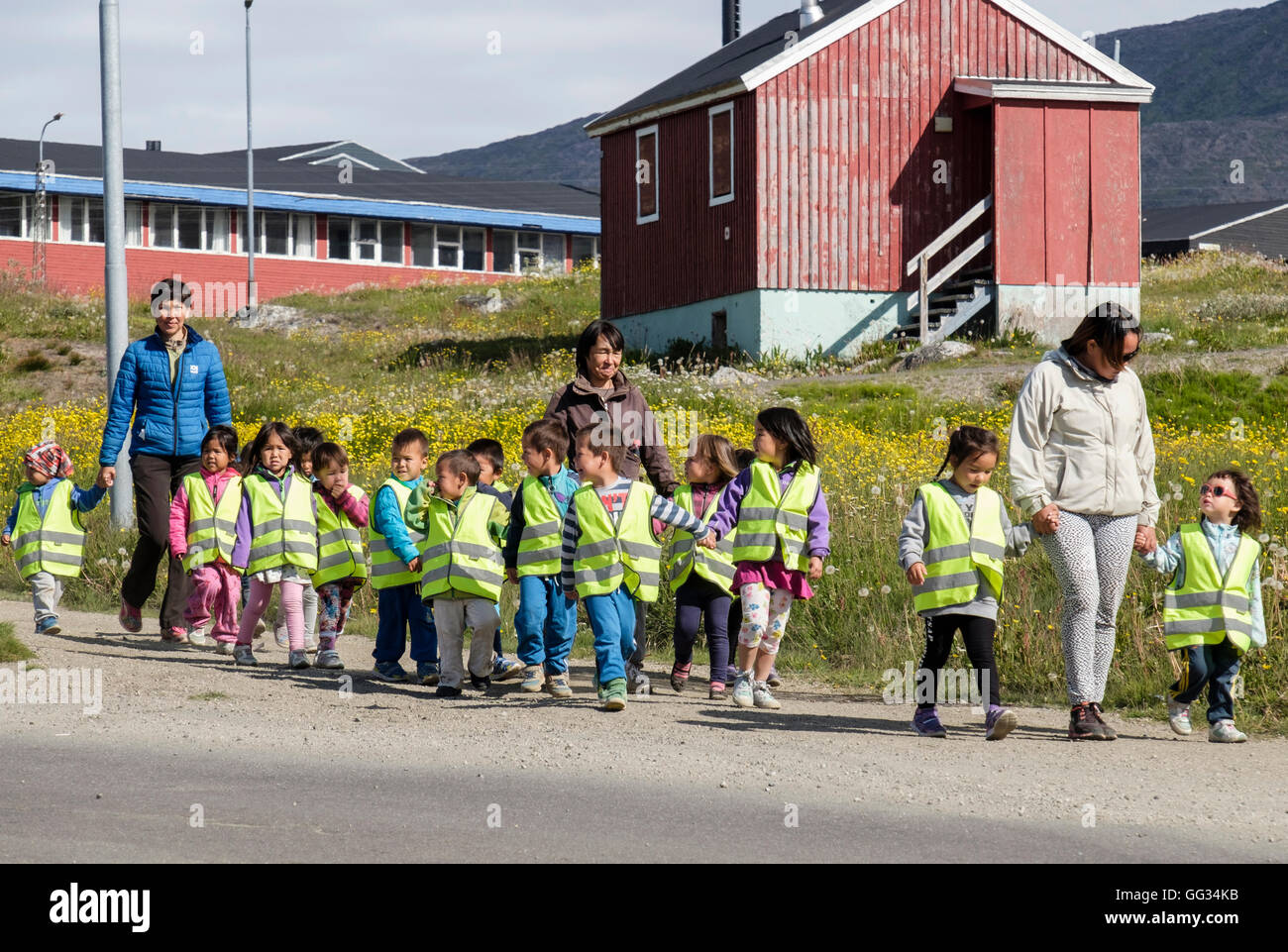 Lokale Schulkinder tragen hi-Vis Jacken und Hand in Hand entlang einer Straße mit ihren Lehrern im Sommer 2016. Narsaq Grönland Stockfoto