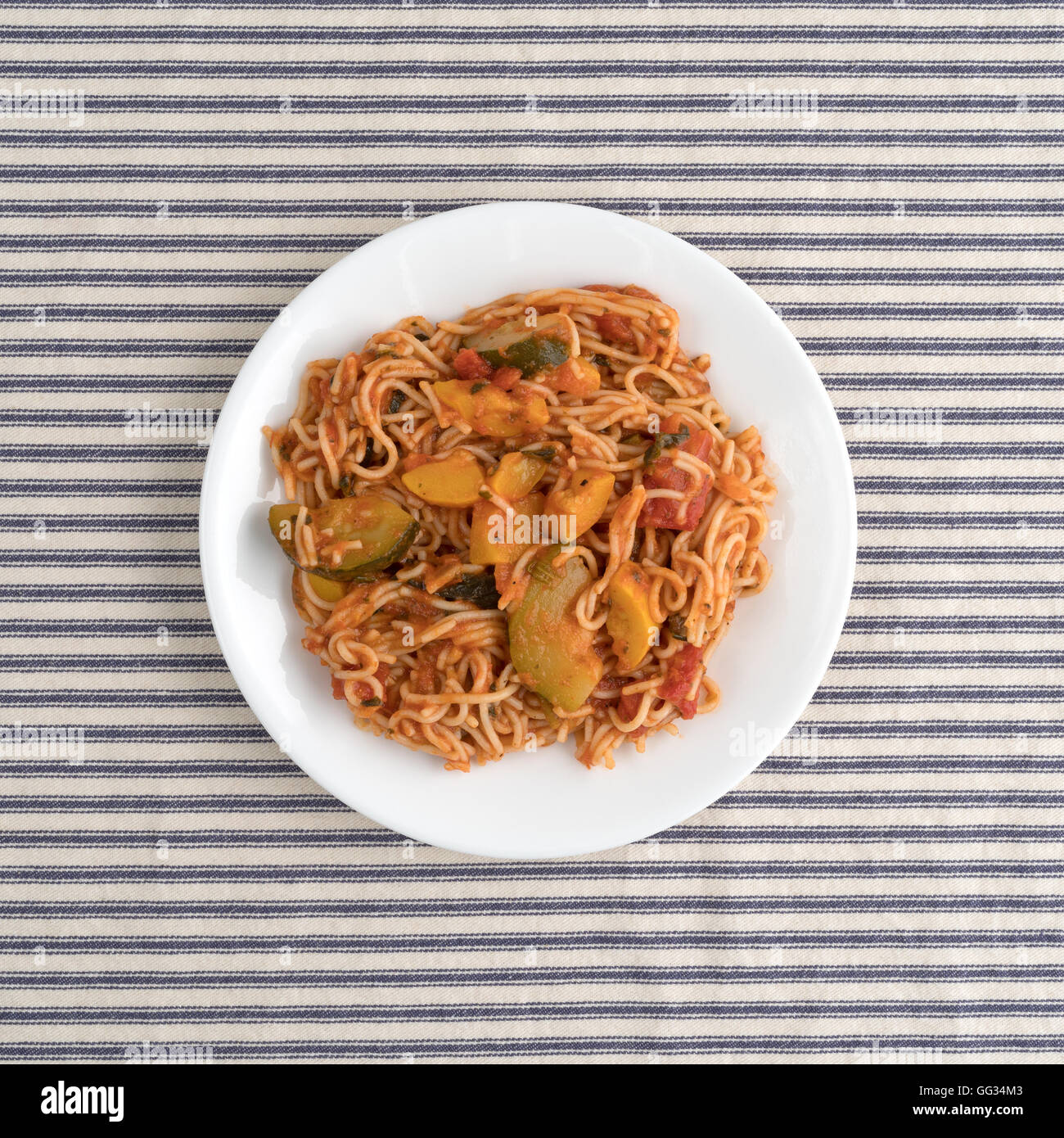 Draufsicht der Engel Haar Pasta mit Zucchini und Spinat auf einem weißen Teller oben auf eine gestreifte Tischdecke. Stockfoto