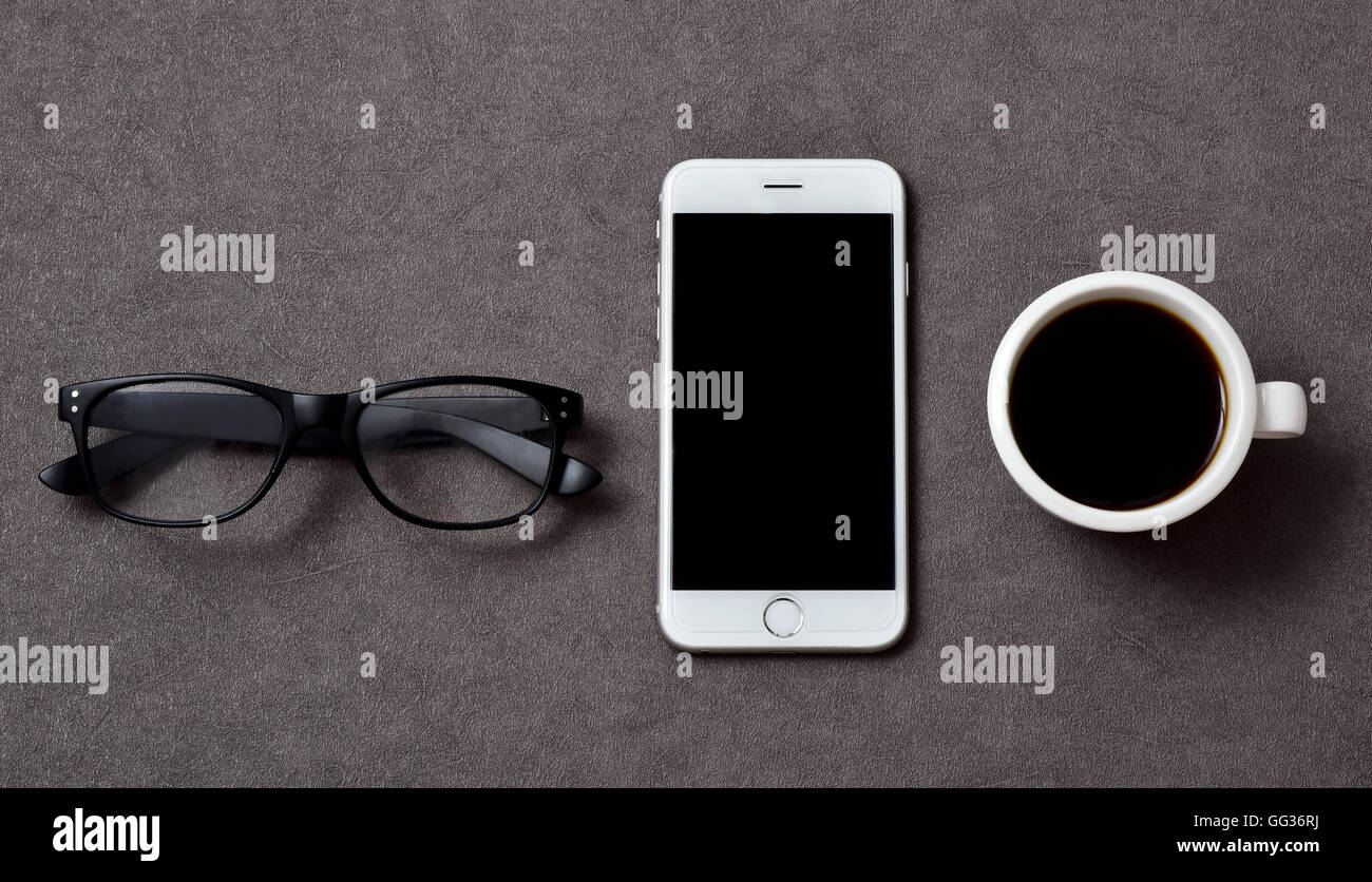 High-Angle Shot von ein paar Brillen, ein Smartphone mit einen schwarzen leere Raum in seinem Bildschirm und eine Tasse Kaffee auf einem eleganten Stockfoto
