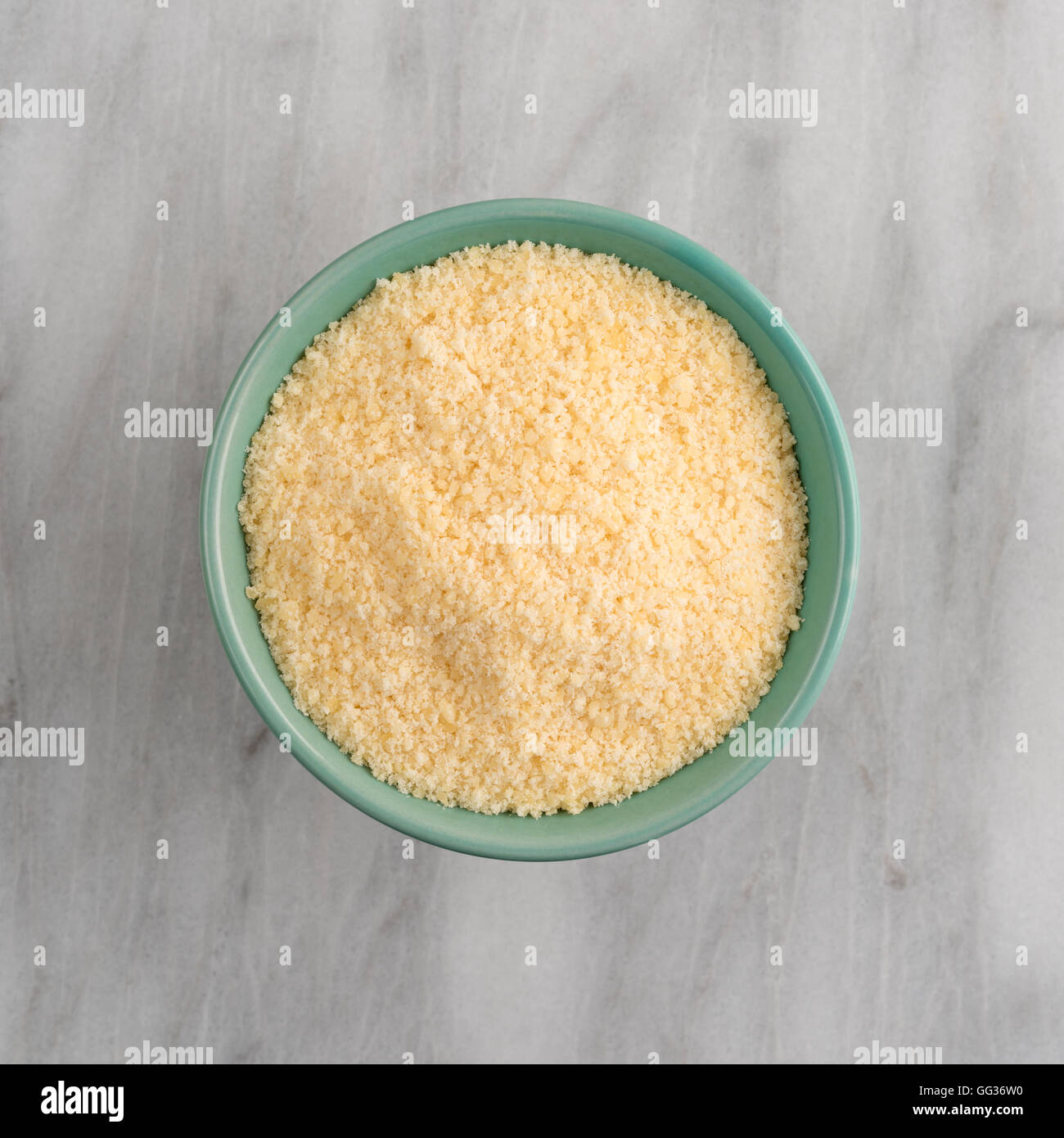 Draufsicht einer grünen Schale gefüllt mit frisch geriebenem Parmesan auf ein Schneidebrett aus Marmor. Stockfoto