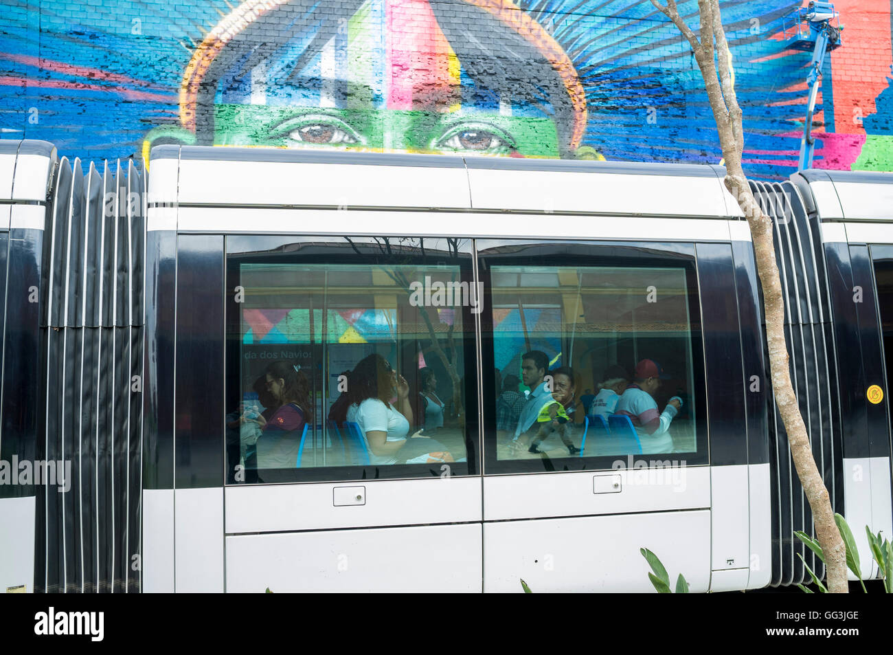 Rio De Janeiro Light Rail (Portugiesisch - VLT do Rio De Janeiro oder VLT Carioca), eine Stadtbahn eröffnet im Juni 2016 vor 2016 Olympischen Spiele Pässe vor Eduardo Kobra s Wandbild benannte Ureinwohner aus 5 Kontinenten (Povos Nativos Dos 5 Continentes) am Boulevard do Porto in Rio De Janeiro Hafen umgebenden Bereich, Brasilien, Teil des Projekts Porto Maravilha (wunderbare Hafen Programm) , ein Revitalisierungsprojekt der Stadt Port Zone. Kobra ist eine brasilianische Street-Artist bekannt für große Wandbilder, Gemälde in der Regel mit Porträts mit einer Technik der Wiederholung Quadrate und trian Stockfoto