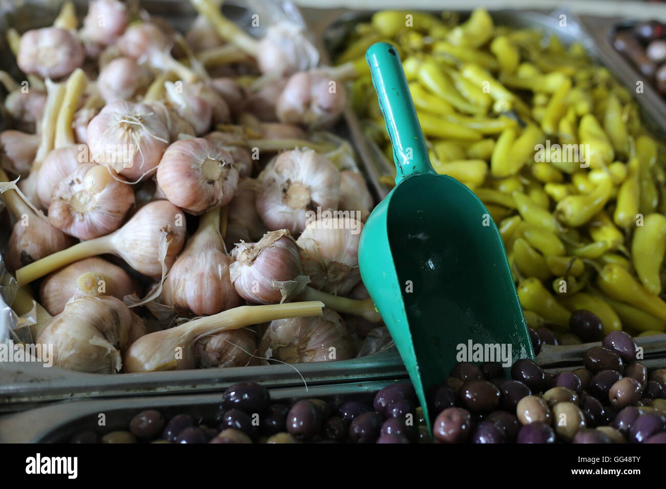 Oliven und Knoblauch. Würzige Oliven, eingelegte Knoblauch Kopf und grüne Chili mit Soße in einem Marktstand. Nahaufnahme von Vorspeisen und Essiggurken Stockfoto