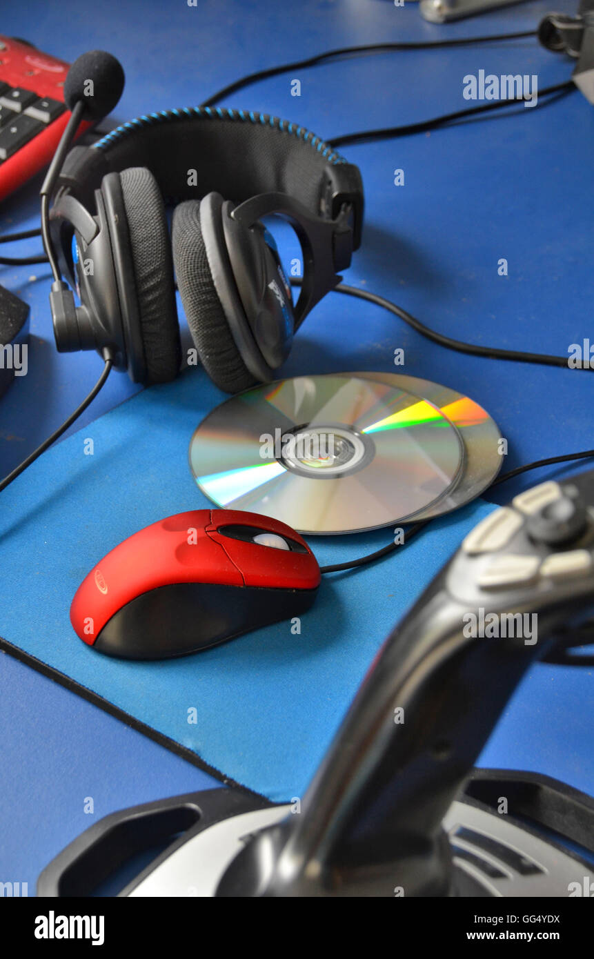 Computer-Desktop mit Gaming-Zubehör wie Kopfhörer, DVDs, Joystick, rote Maus und Matte. Stockfoto