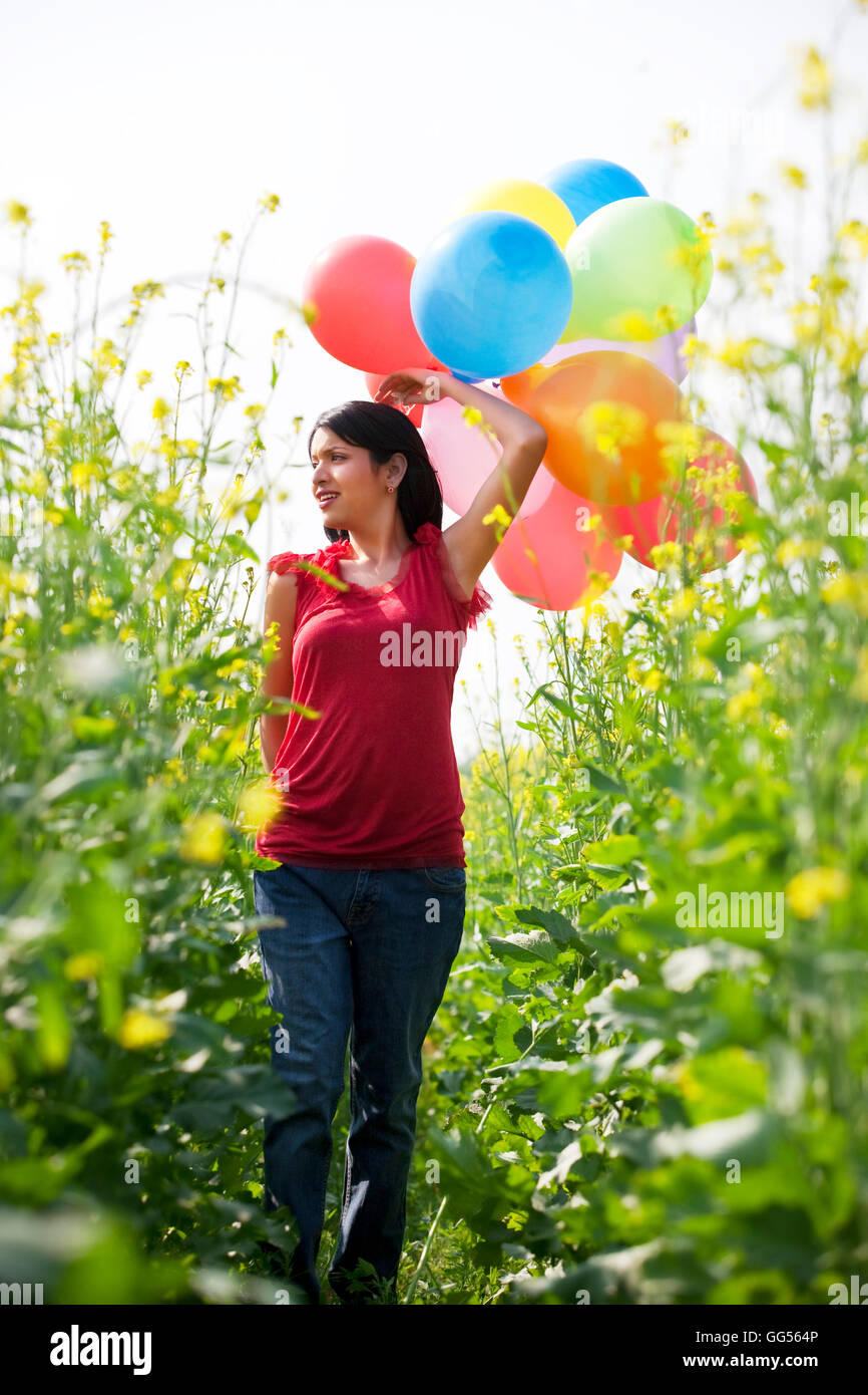 Junge Frau mit Luftballons zu Fuß in ein Feld Stockfoto
