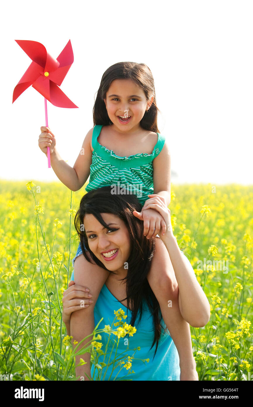 Mädchen mit einem Windrad auf ihre Mütter Schultern sitzen Stockfoto