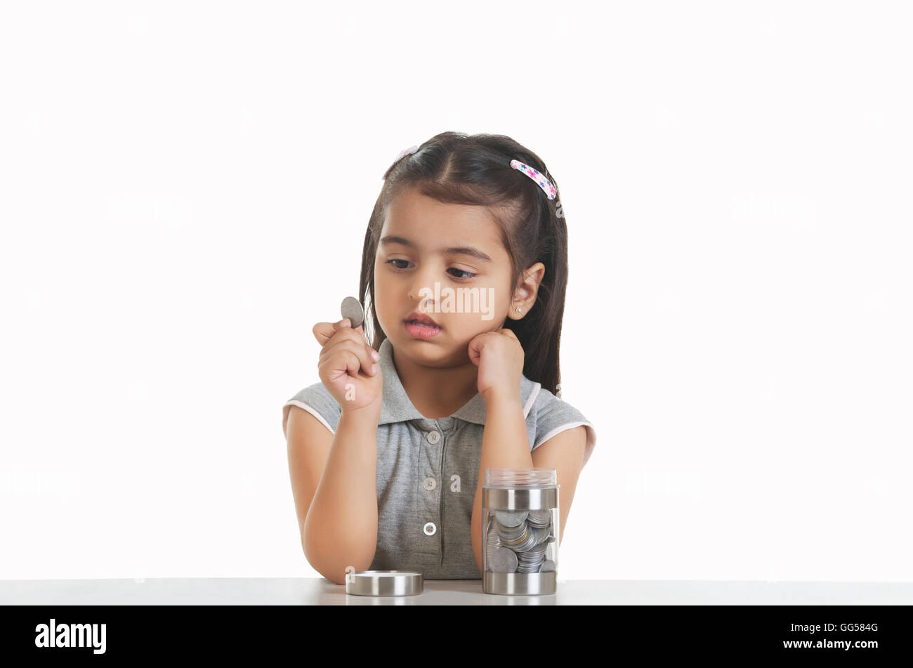 Niedliche Mädchen indische Münze beim Sitzen am Tisch vor weißem Hintergrund halten Stockfoto