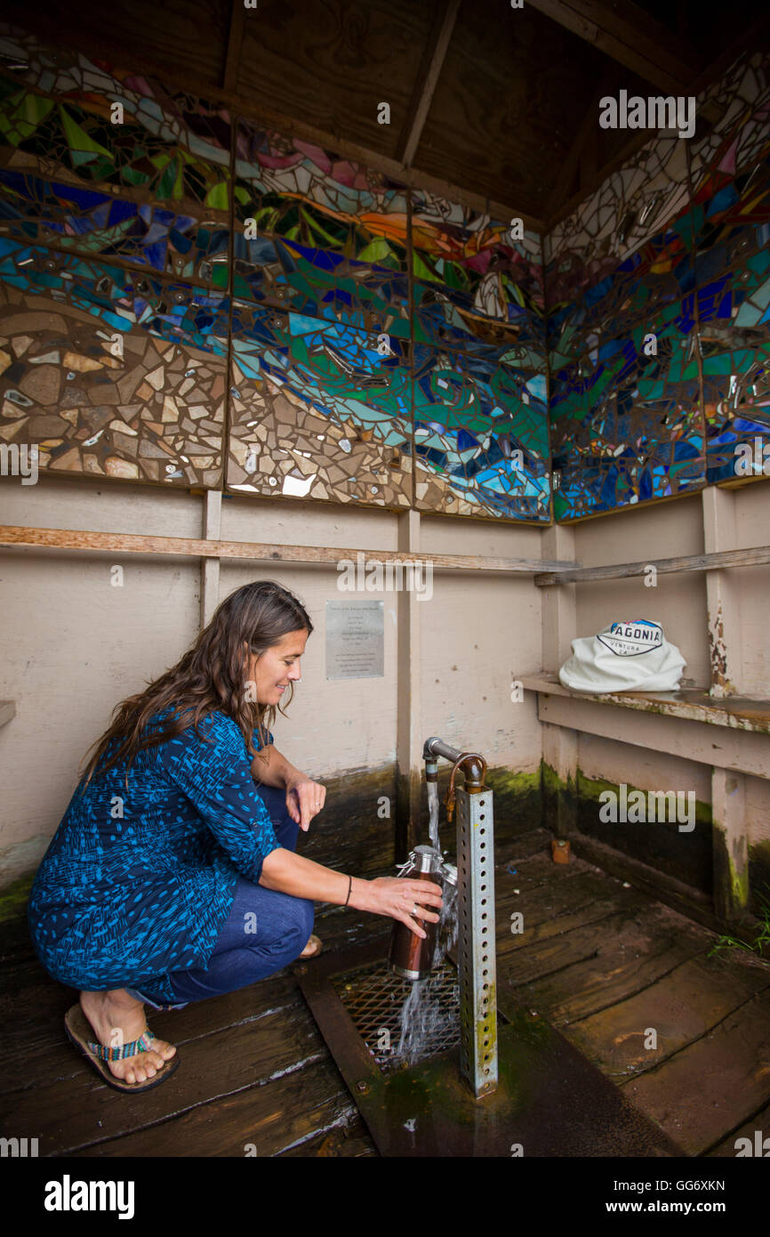 Eine erwachsene Frau füllt eine Flasche Resusable Wasser bei einem artesischen Brunnen. Stockfoto