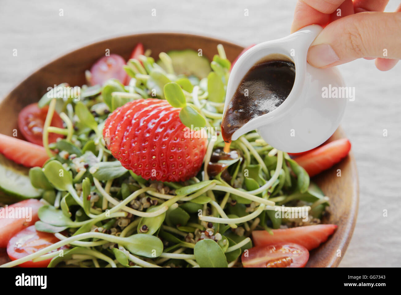 Gießen Dressing auf Sonnenblumen Salat mit Sprossen und Erdbeeren auf Holzschale Stockfoto