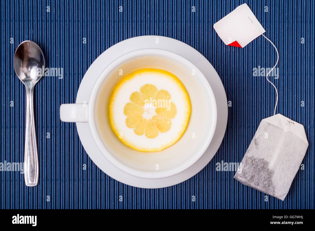 einfache Zusammensetzung mit Teetasse leer, aber mit Scheibe Zitrone, Untertasse und Löffel, filter Beutel mit tessu blau gestreiften Hintergrund Stockfoto