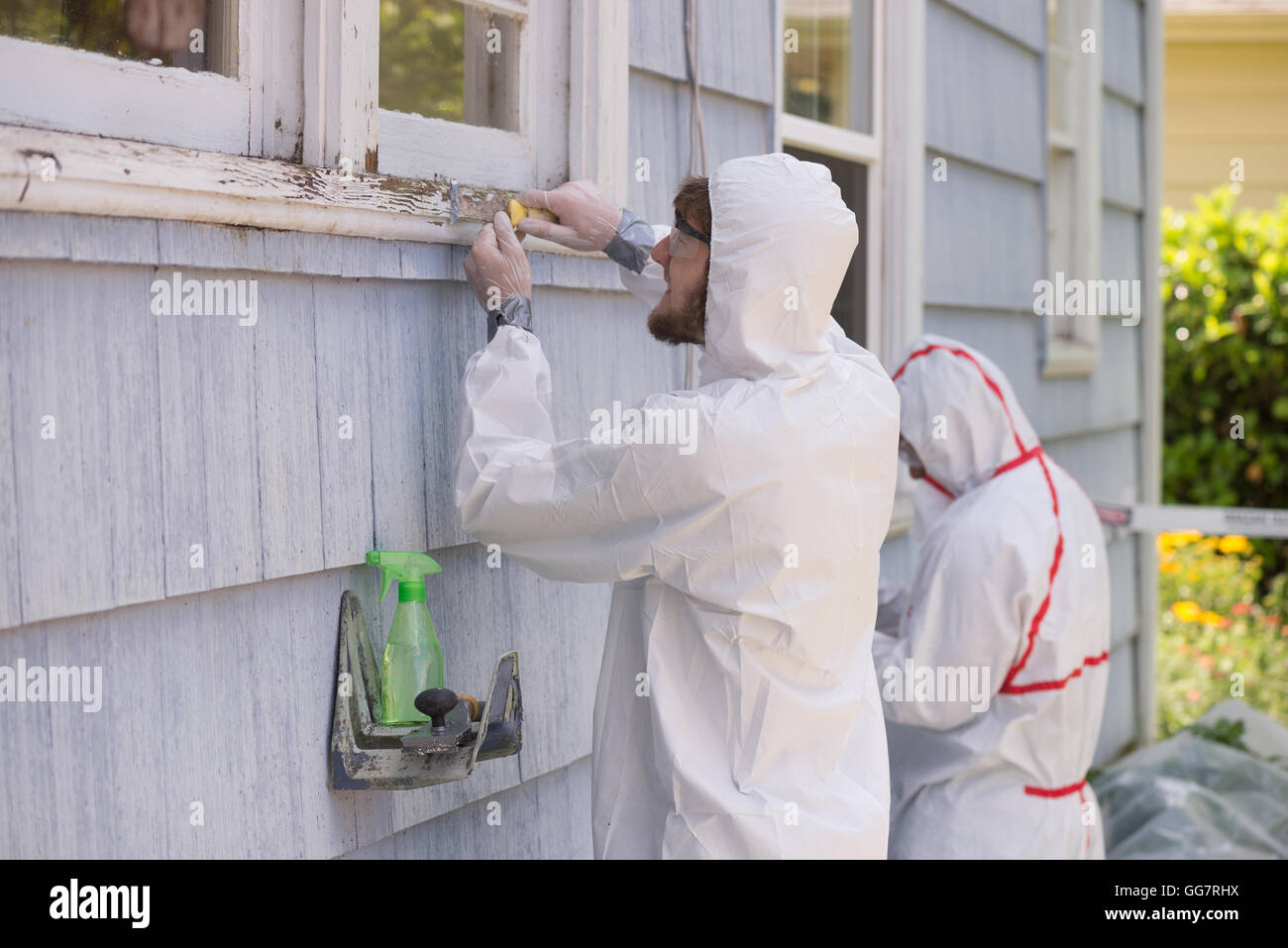 Zwei Hausmaler in Hazmat Anzügen entfernen Blei malen von einem alten Haus. Stockfoto