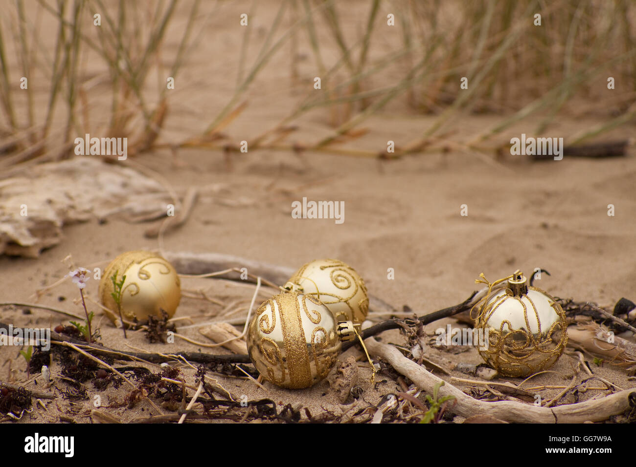 Dekorative Weihnachtskugeln in Sand mit Treibholz an einem Strand in Neuseeland für einen Sommer der Südhalbkugel Xmas angeordnet Stockfoto