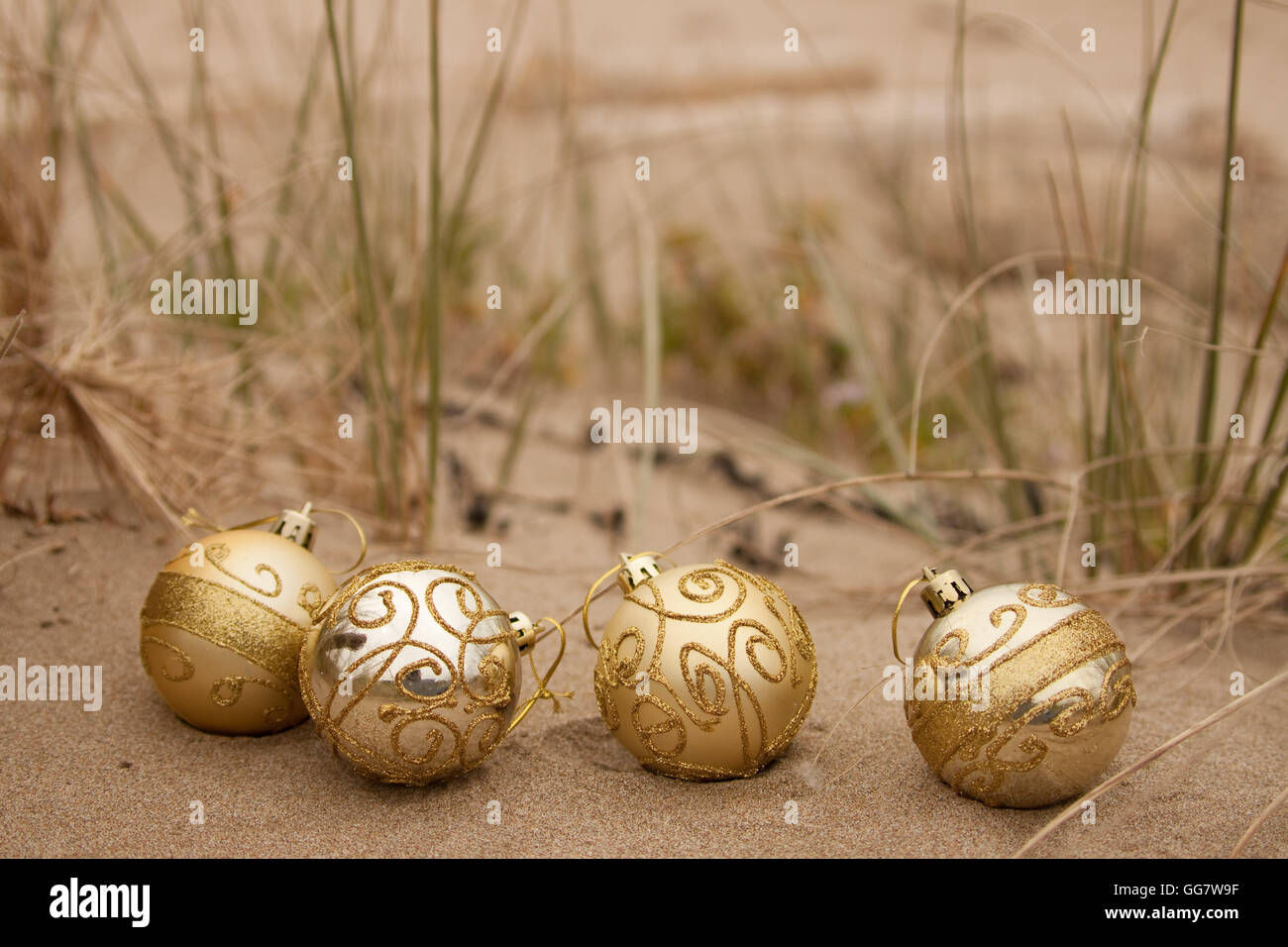 Dekorative Weihnachtskugeln in Sand mit Treibholz an einem Strand in Neuseeland für einen Sommer der Südhalbkugel Xmas angeordnet Stockfoto