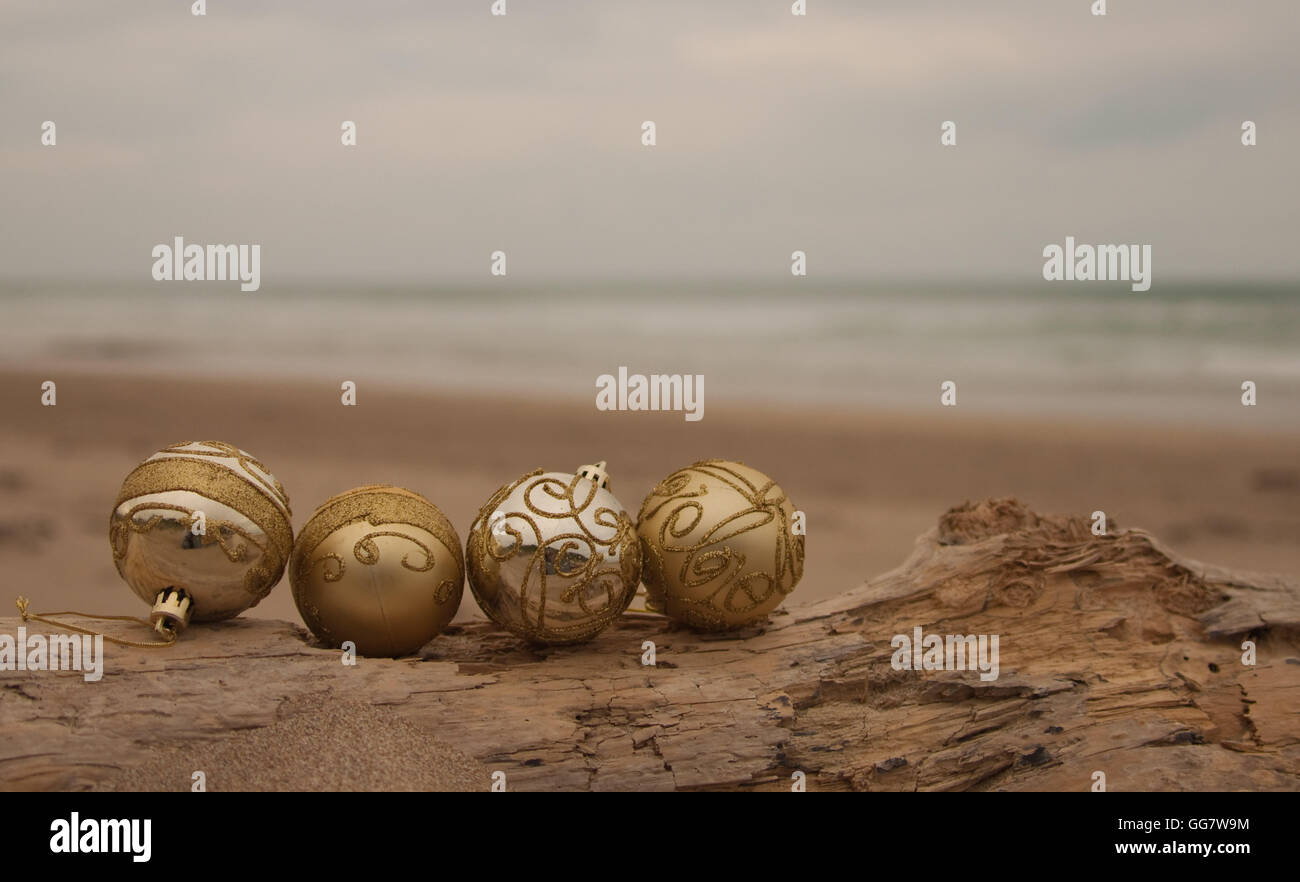 Dekorative Weihnachtskugeln in Sand mit Treibholz an einem Strand in Neuseeland für einen Sommer der Südhalbkugel Xmas angeordnet Stockfoto