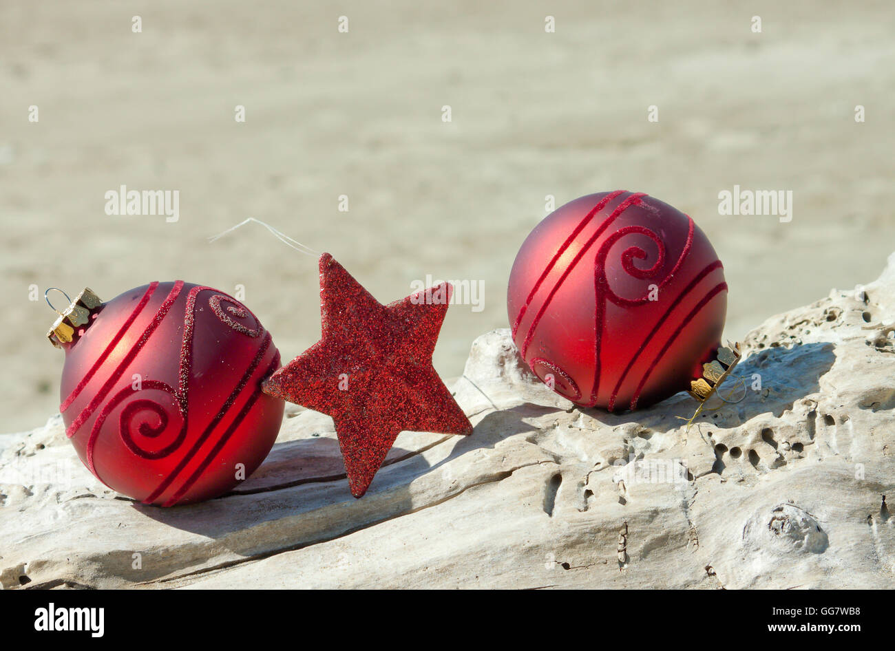 Dekorative Weihnachtskugeln in Sand mit Treibholz an einem Strand in Neuseeland für einen Sommer der Südhalbkugel Xmas angeordnet Stockfoto
