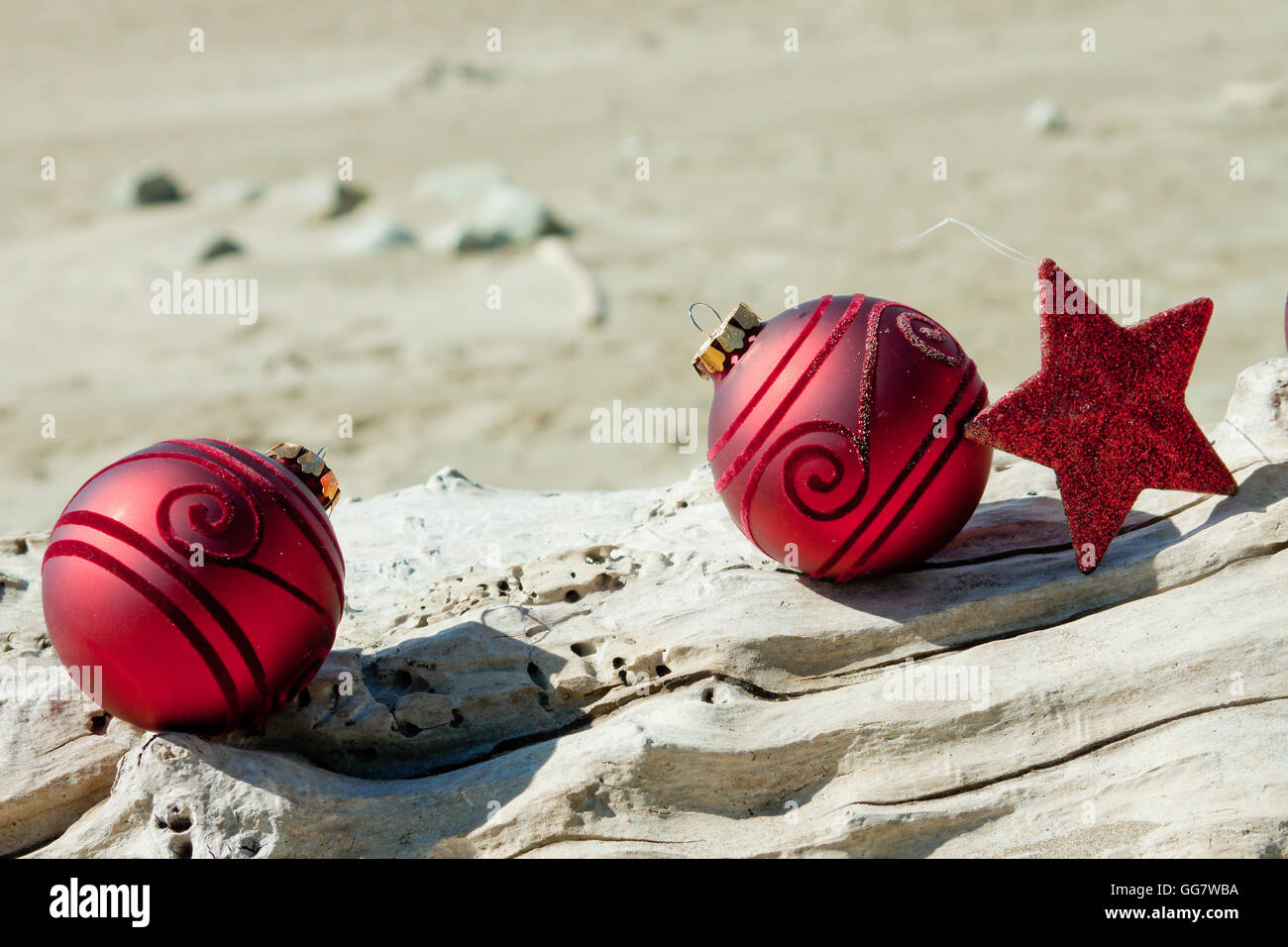 Dekorative Weihnachtskugeln in Sand mit Treibholz an einem Strand in Neuseeland für einen Sommer der Südhalbkugel Xmas angeordnet Stockfoto
