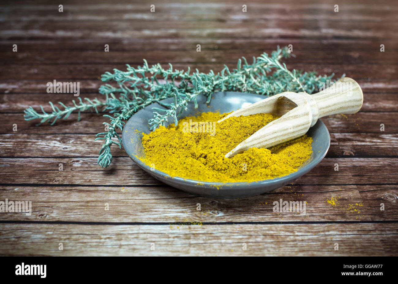 Kleinen Teller mit Curry-Pulver mit einem Holzlöffel Stockfoto