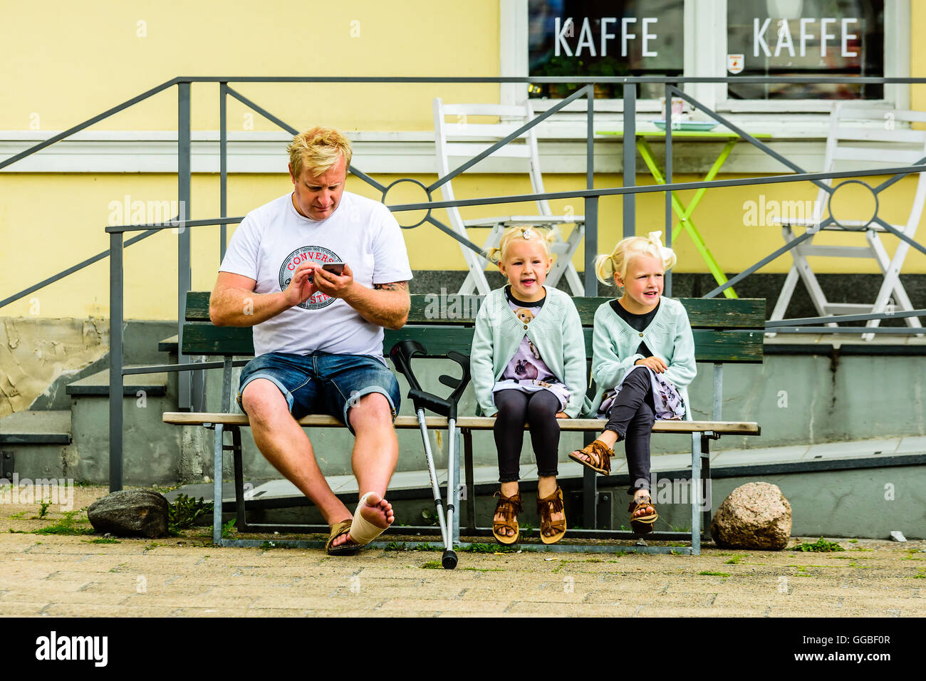 Ystad, Schweden - 1. August 2016: Echte Menschen im Alltag. Erwachsener Mann mit Krücken und einem verletzten Fuß sitzen neben zwei schöne Mädchen Stockfoto