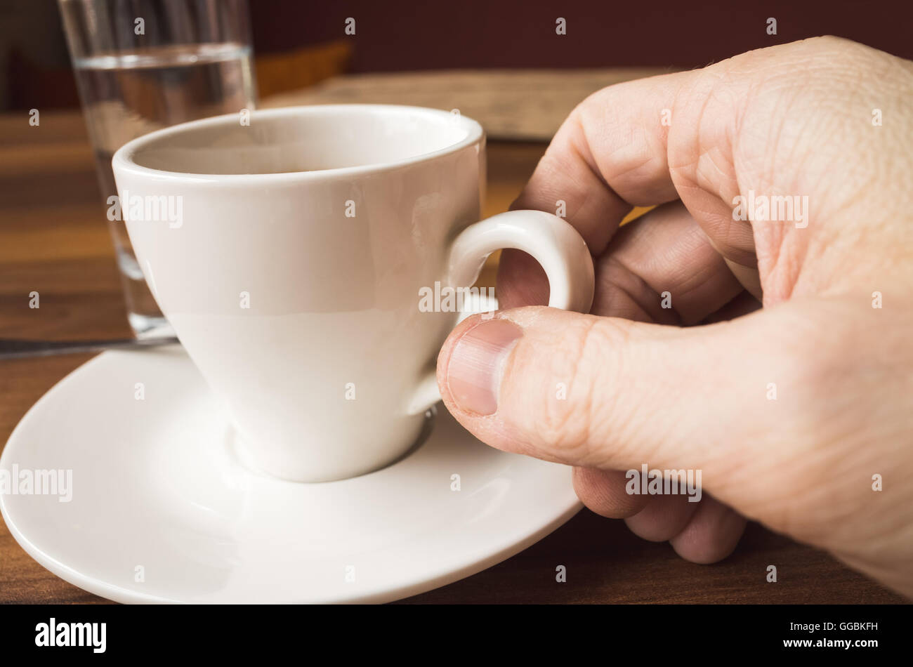Männliche Hand hält weiße Tasse Espresso. Nahaufnahme Foto mit selektiven Fokus Stockfoto