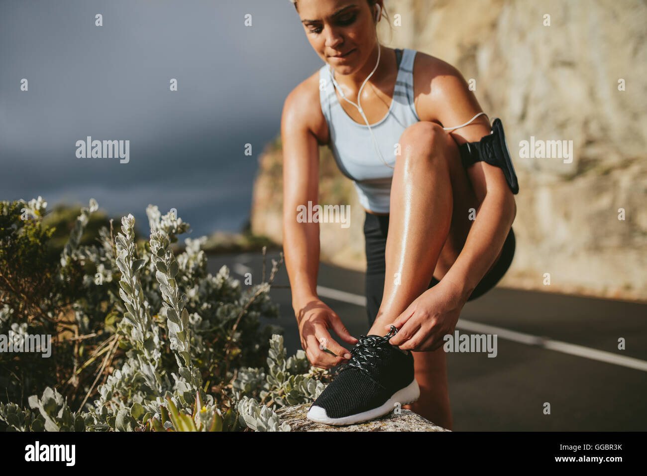 Frau schnürt Laufschuhe im Freien auf der Landstraße. Fitness und gesundes Lifestyle-Konzept. Stockfoto