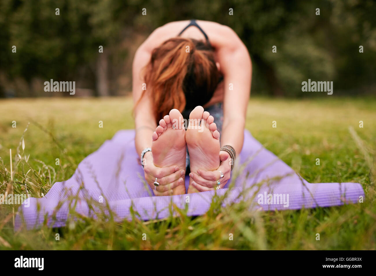 Junge Frau, die im Freien Yoga auf Gras macht, Paschimottanasana-Pose übt. Fitness-Frau sitzend nach vorne beugen während des Trainings Stockfoto