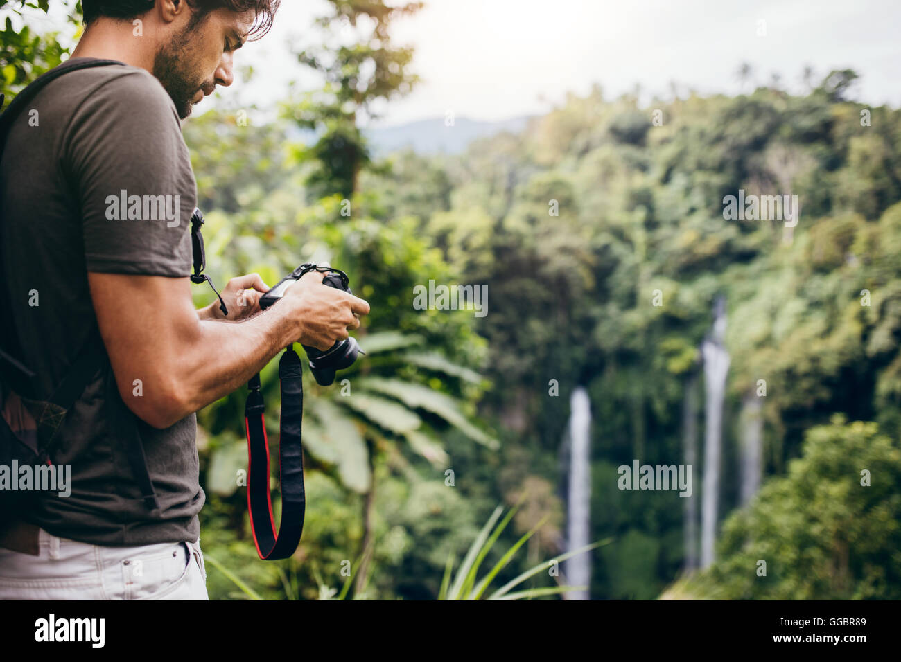 Mann stand vor Wasserfall mit Digitalkamera und überprüfen die Bilder. Männliche Wanderer fotografieren einen Wasserfall in fores Stockfoto