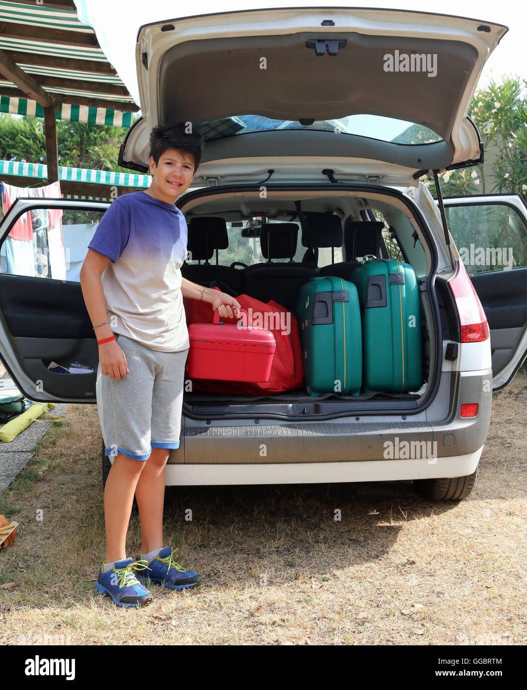 Junge hilft den Kofferraum des Autos laden vor der Abreise nach einer langen Reise Stockfoto
