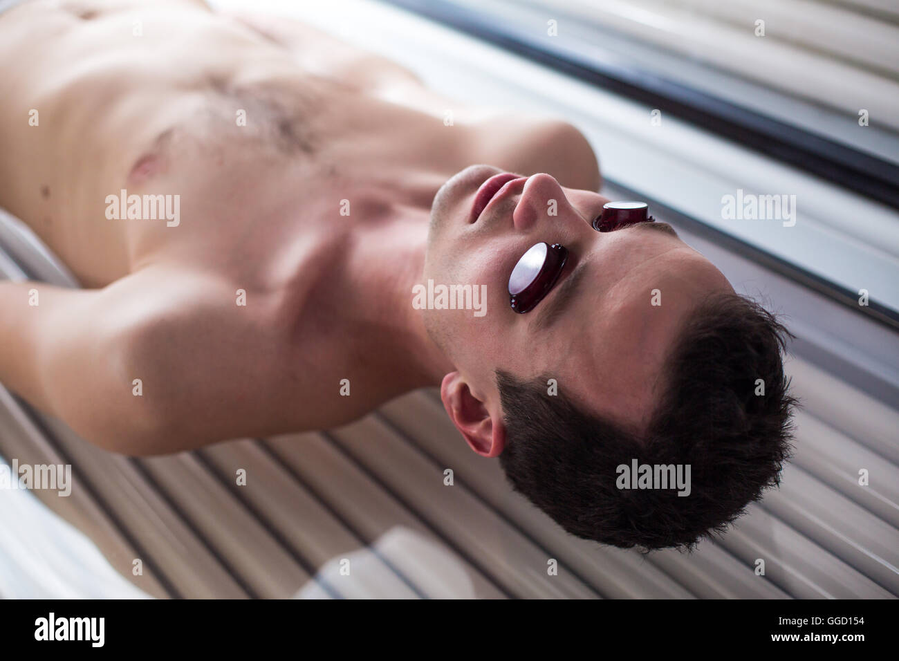 Hübscher junger Mann während einer Bräunungssitzung in ein modernes Solarium entspannen, kümmert sich um sich selbst, genießen die künstliche Stockfoto