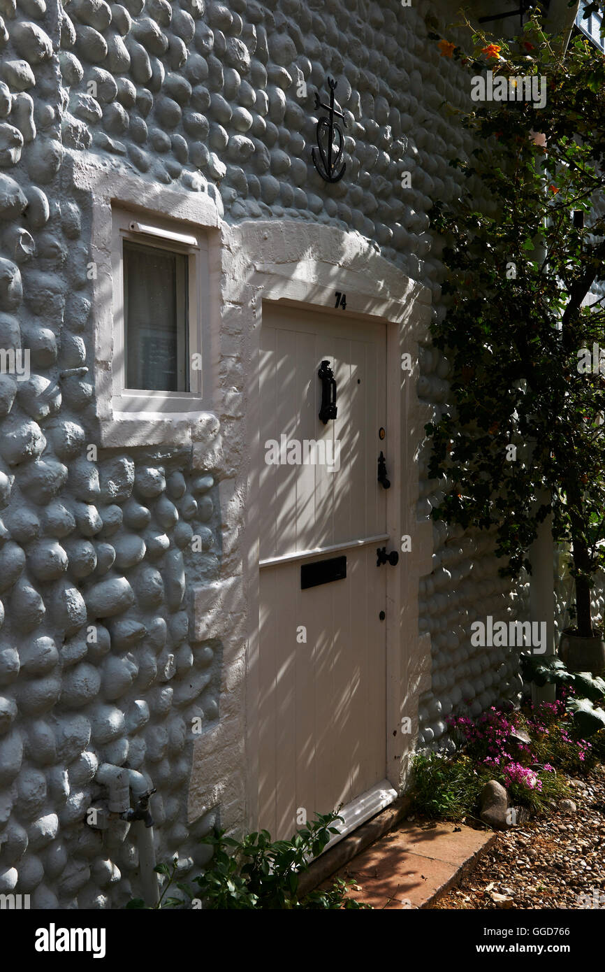 Cream Ferienhaus Tür inmitten einer großen gepflasterten Mauer, mit schwarzen Türknauf und Klopfer mit gesprenkelten Sonnenlicht auf sie geworfen. Stockfoto