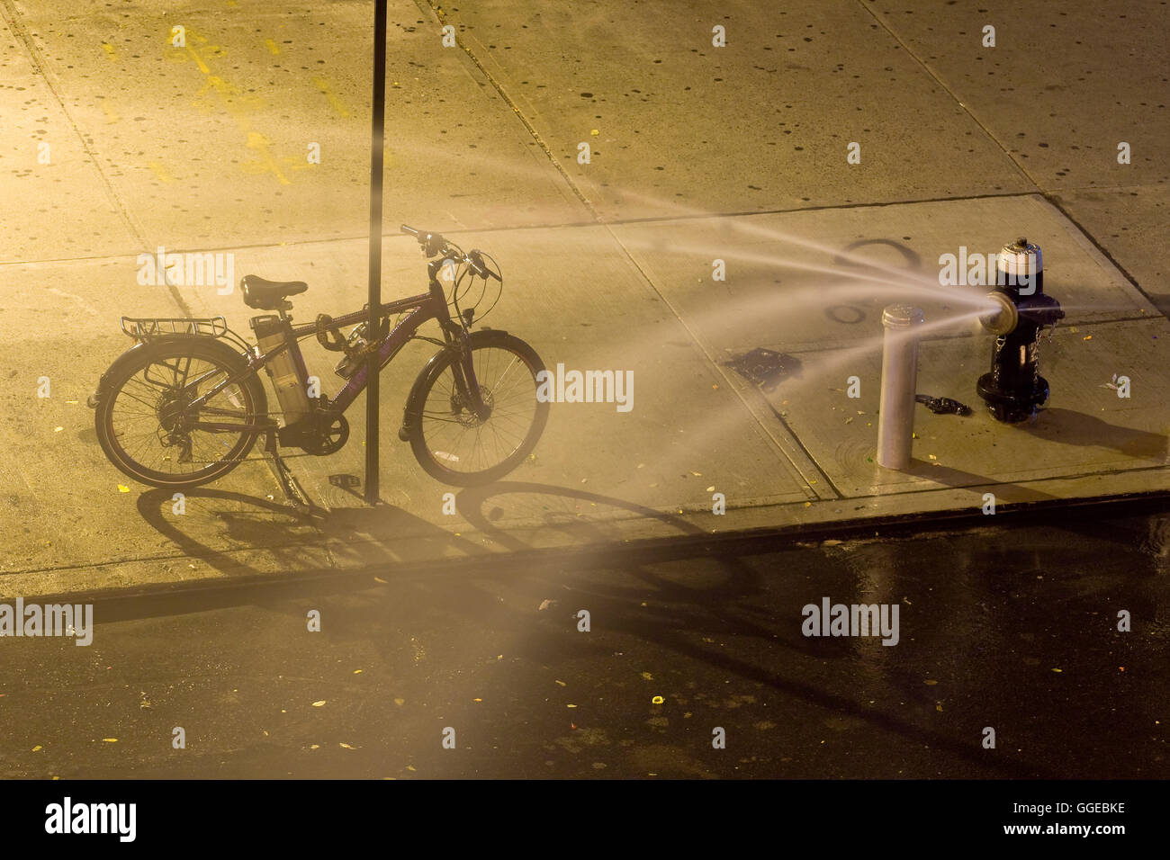 Offenen Hydranten mit Kappe Spritzdüse schießen Ströme von Wasser hinter dem Fahrrad angekettet an einen Pfahl in einer heißen Sommernacht Stockfoto