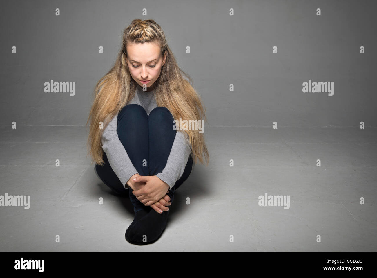 Traurige junge Frau sitzt im leeren Raum am Boden Hände umwickelt Beine blickte Konzept Stockfoto