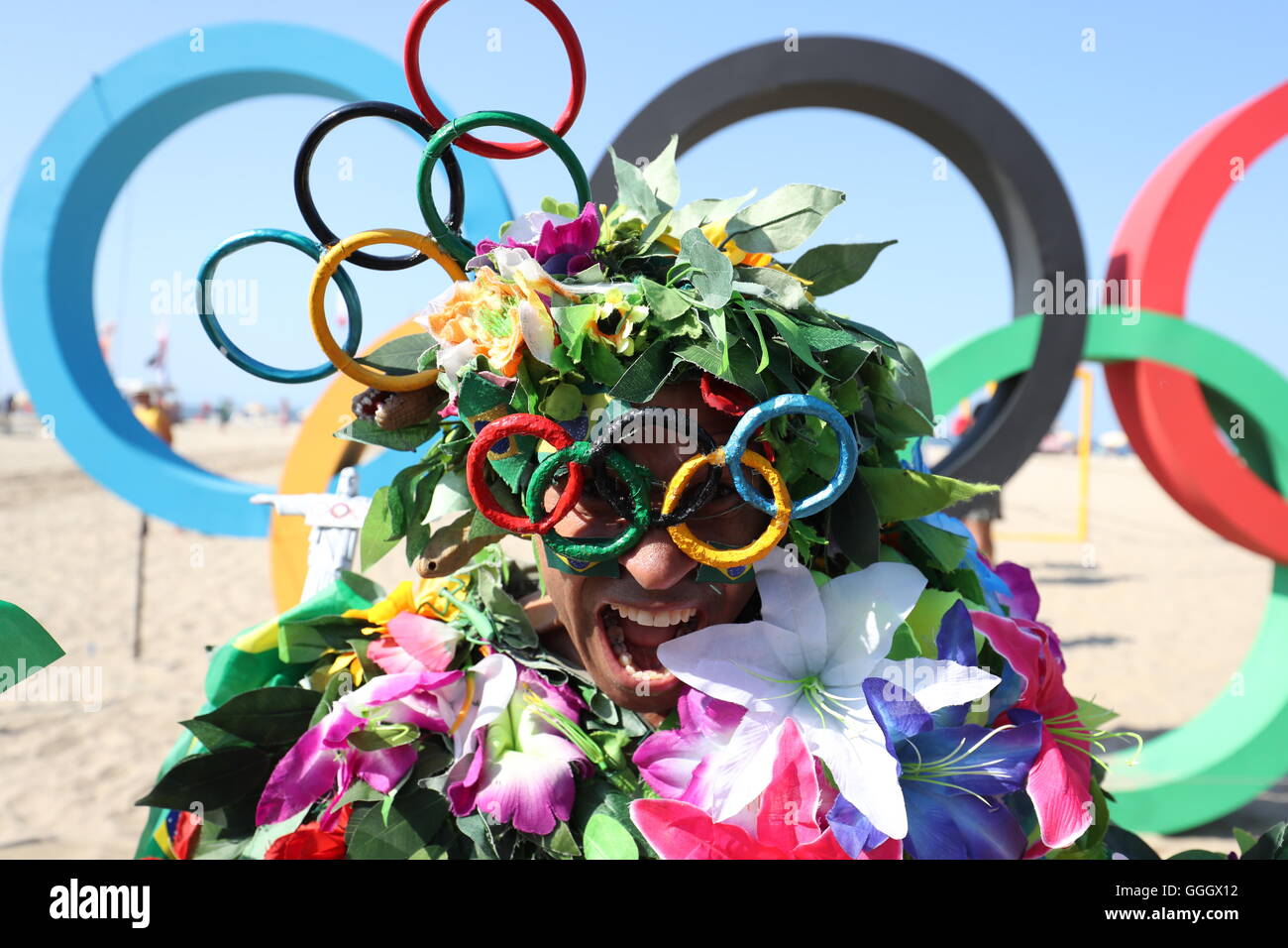 Ein Mann bedeckt in Blumen posiert für ein Foto vor der Olympischen Ringe an der Copacabana, Rio De Janeiro, Brasilien. Stockfoto