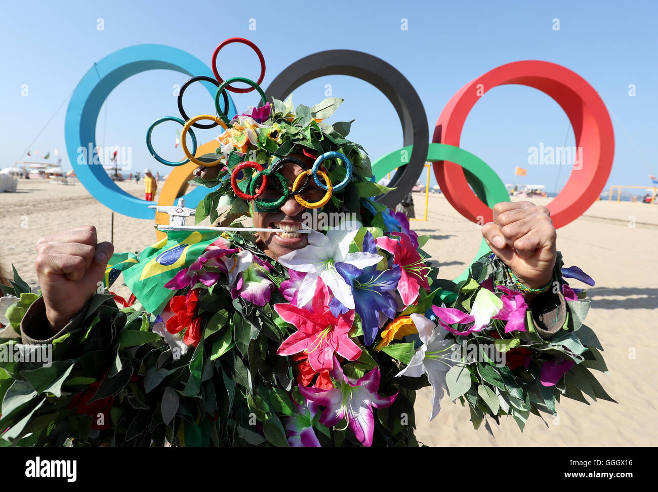 Ein Mann bedeckt in Blumen posiert für ein Foto vor der Olympischen Ringe an der Copacabana, Rio De Janeiro, Brasilien. Stockfoto