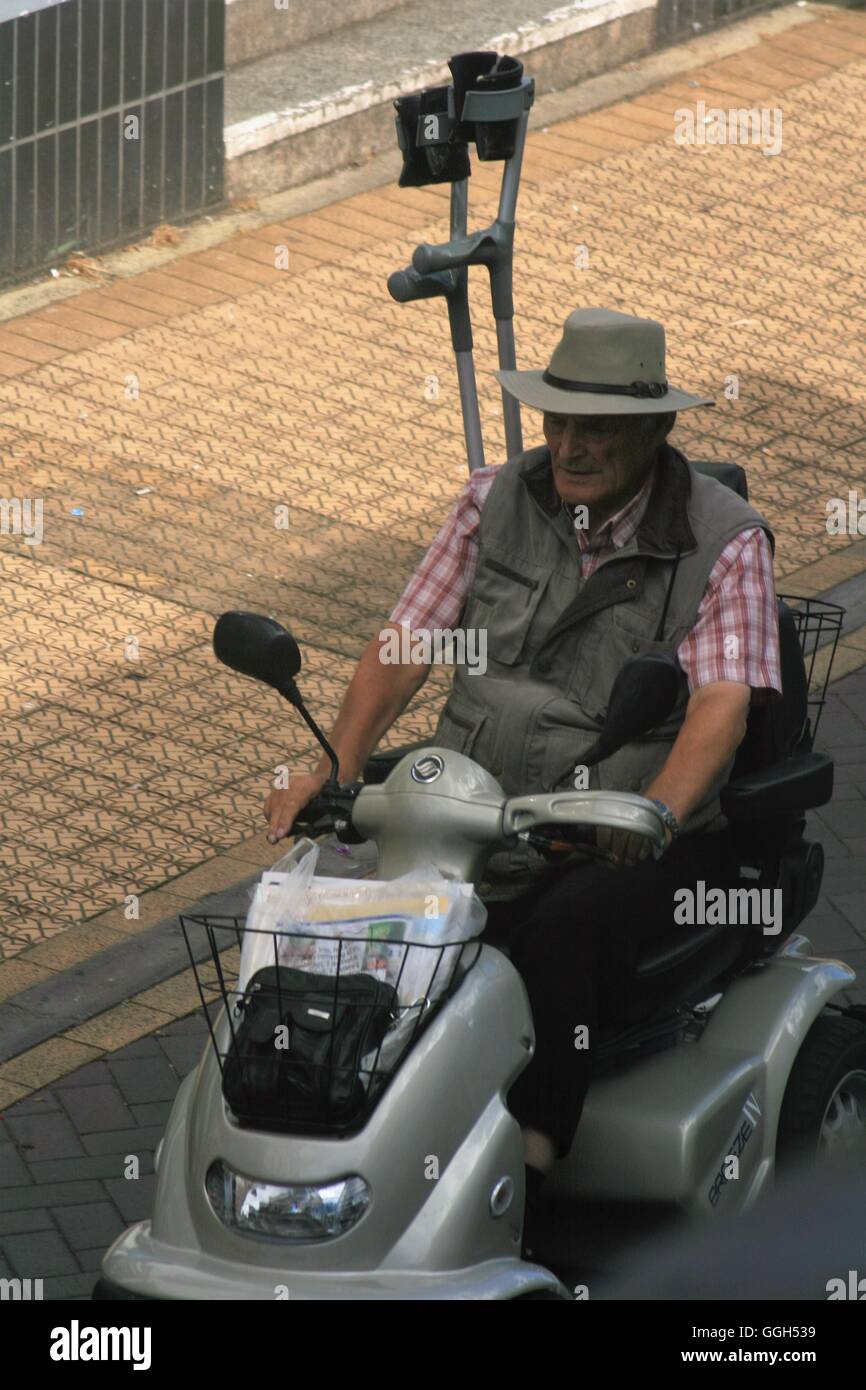 älterer Mann fahren durch die Stadt auf einem Elektromobil mit Krücken in der Rückseite gespeichert Stockfoto