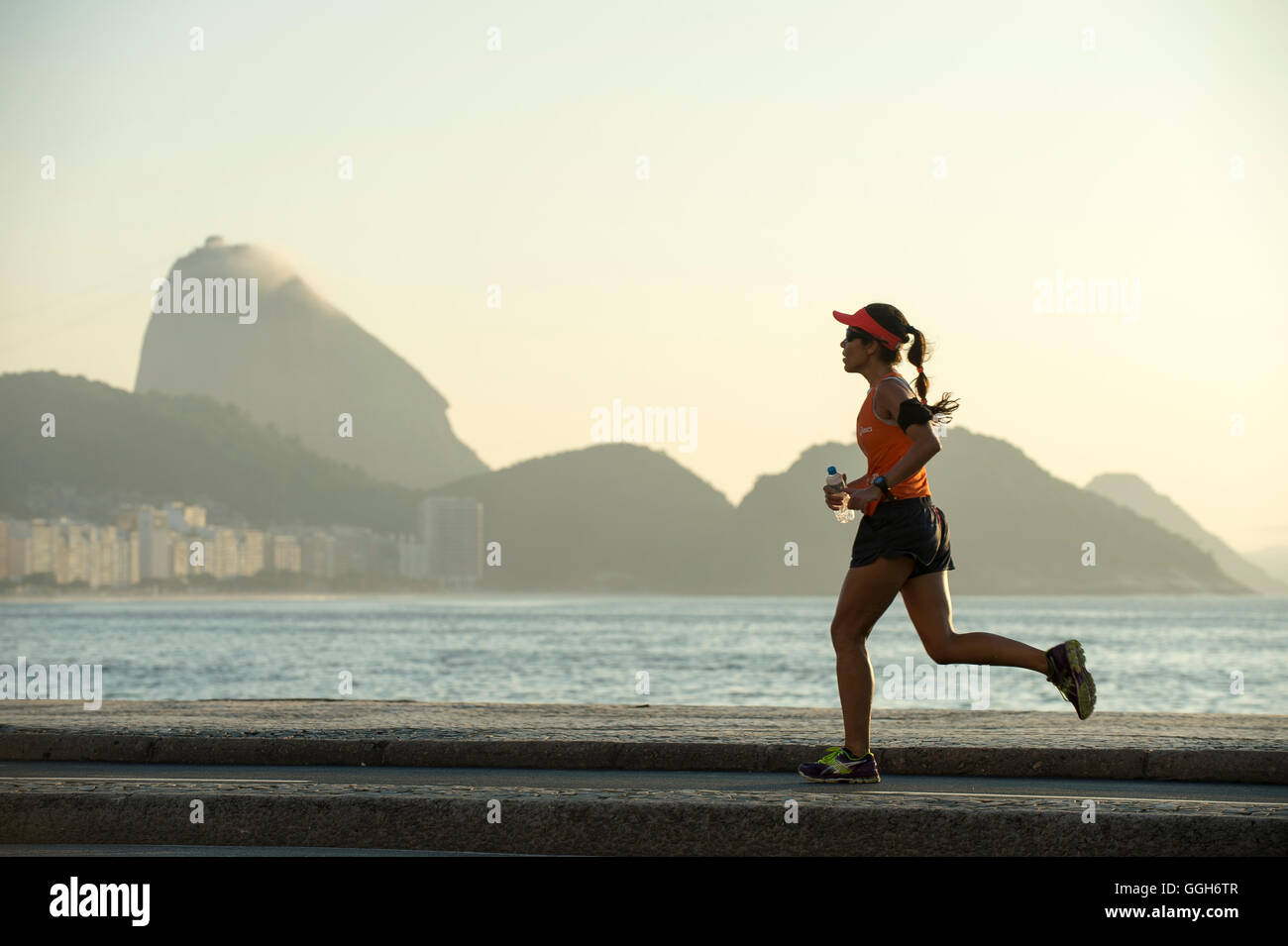 RIO DE JANEIRO - 3. April 2016: Ein Jogger auf der Copacabana Promenade verläuft vor der Silhouette der Zuckerhut. Stockfoto