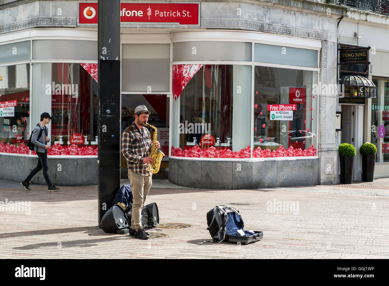 Ein Straßenmusikant spielt das Saxophon außerhalb Vodafone, Patrick Street, Cork, Irland. Stockfoto