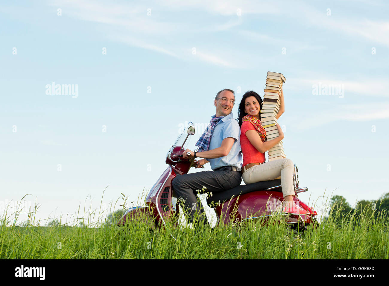 Ein Mann und eine Frau, die Transport von einem Stapel Bücher auf einem roten Vespa Roller, Bad Wildungen, Hessen, Deutschland, Europa Stockfoto