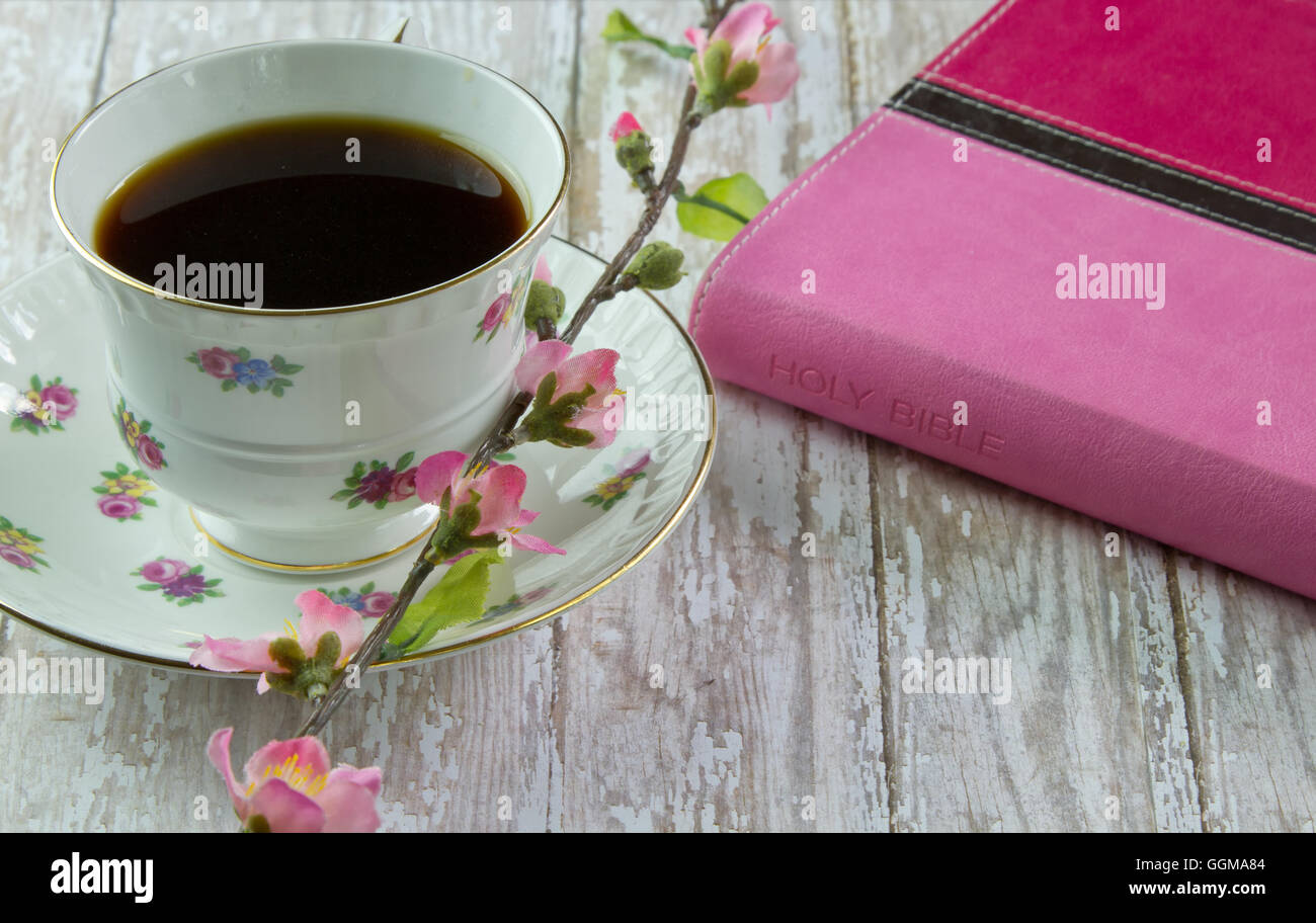Ein rosa Bibel auf einem Holzbrett Brett mit einer Tasse Kaffee oder Tee, umgeben von rosa Frühlingsblumen Stockfoto