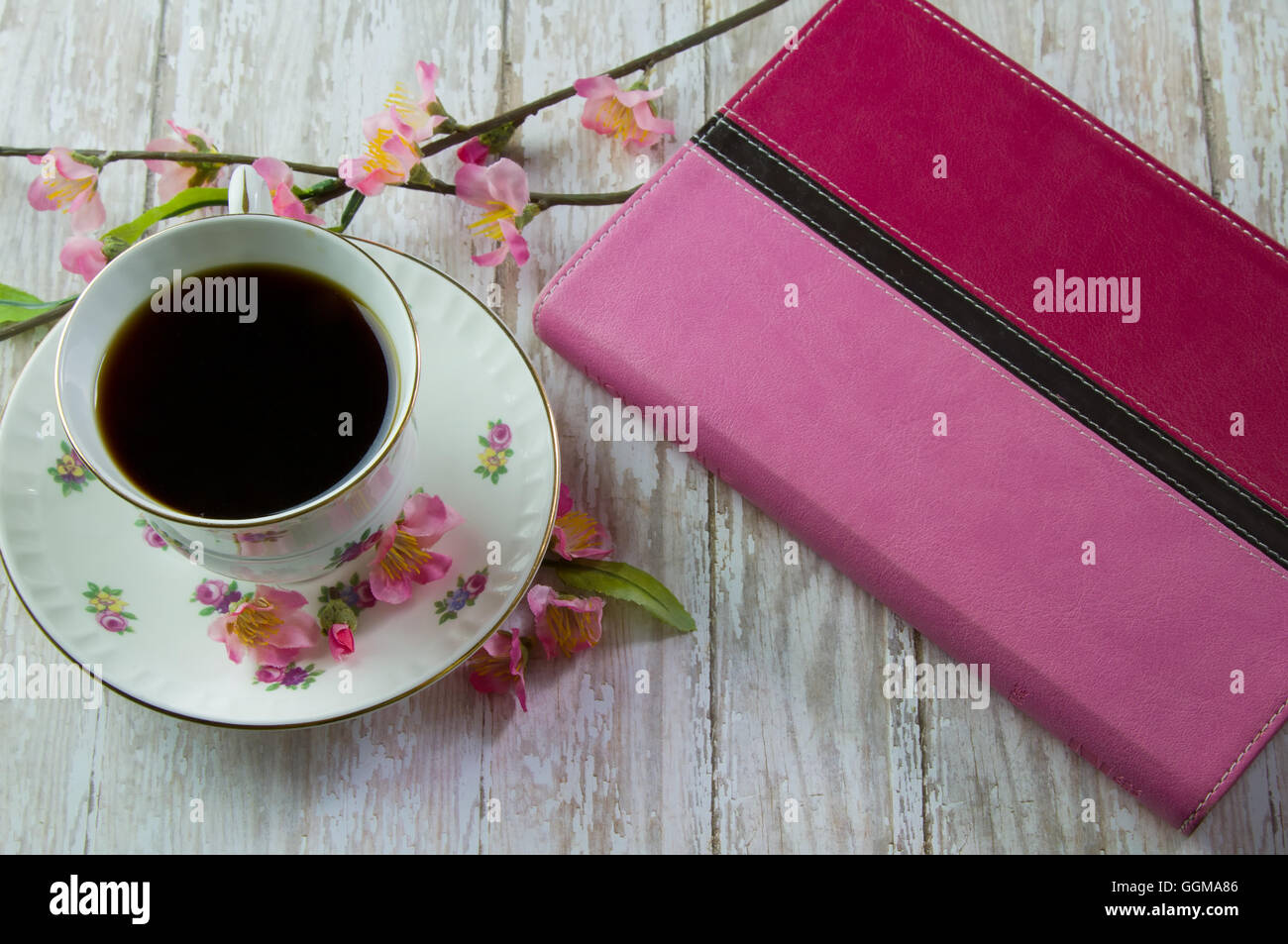 Ein rosa Bibel auf einem Holzbrett Brett mit einer Tasse Kaffee oder Tee, umgeben von rosa Frühlingsblumen Stockfoto