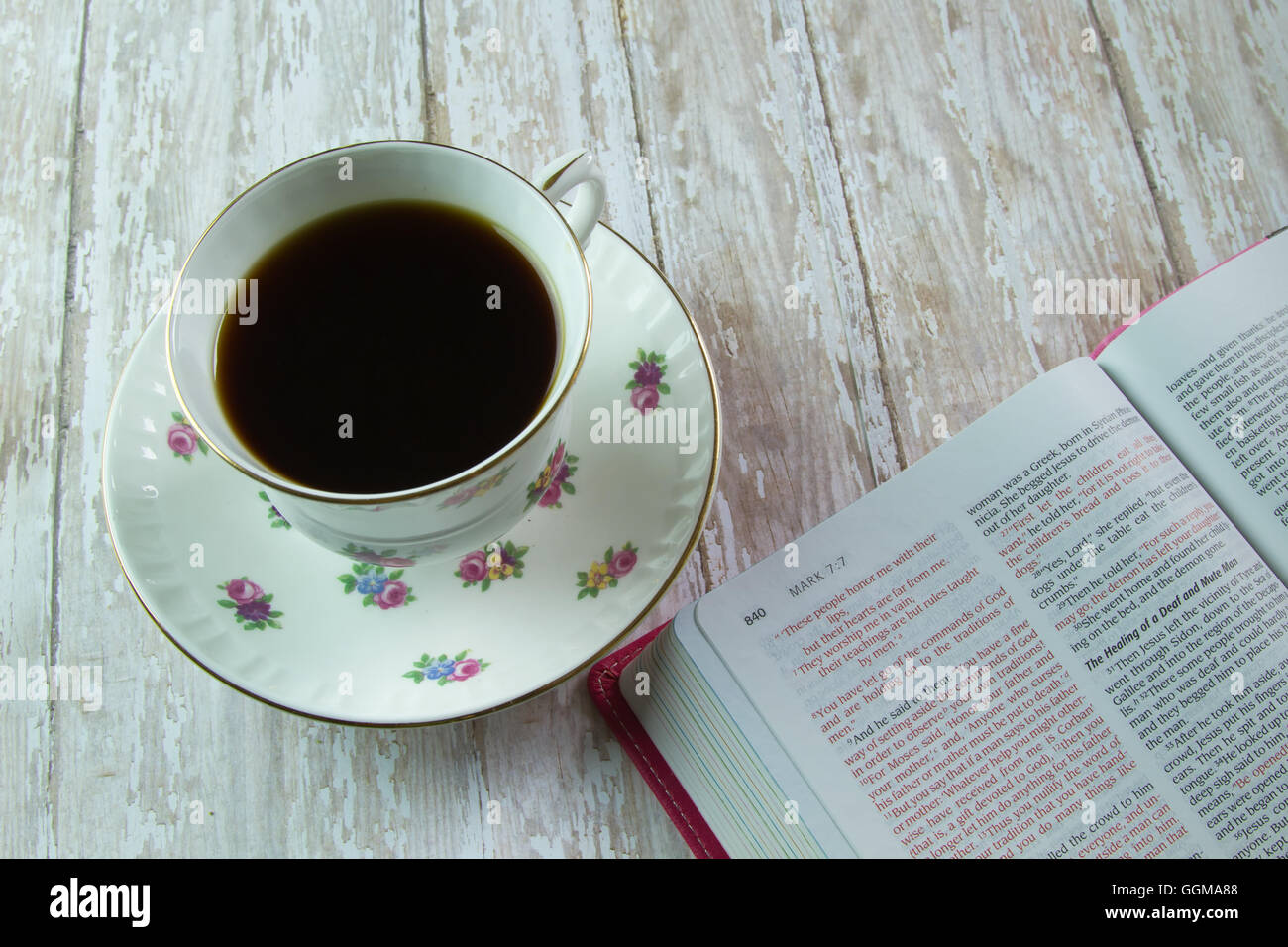 Die Heilige Bibel öffnete sich das Buch von Mark mit einer blühenden Teetasse mit Kaffee oder Tee gefüllt Stockfoto
